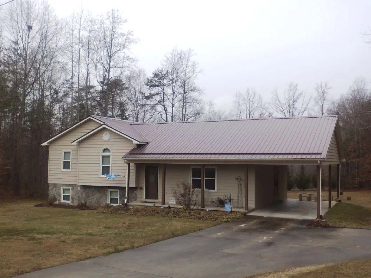 Burgundy metal roof on a tan split level home with an attached carport in Youngsville