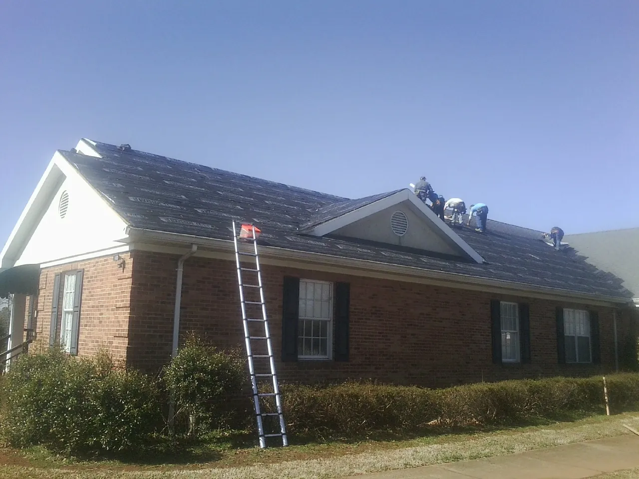 Crew tearing shingles off a brick ranch roof with a ladder set — Emergency Roof Repair work by our crew in Youngsville