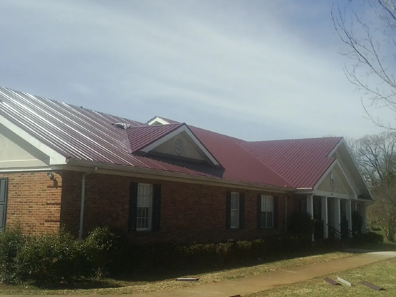 Red metal roof with gabled entries on a long brick building, from a Hail Damage Roof Repair job in Youngsville
