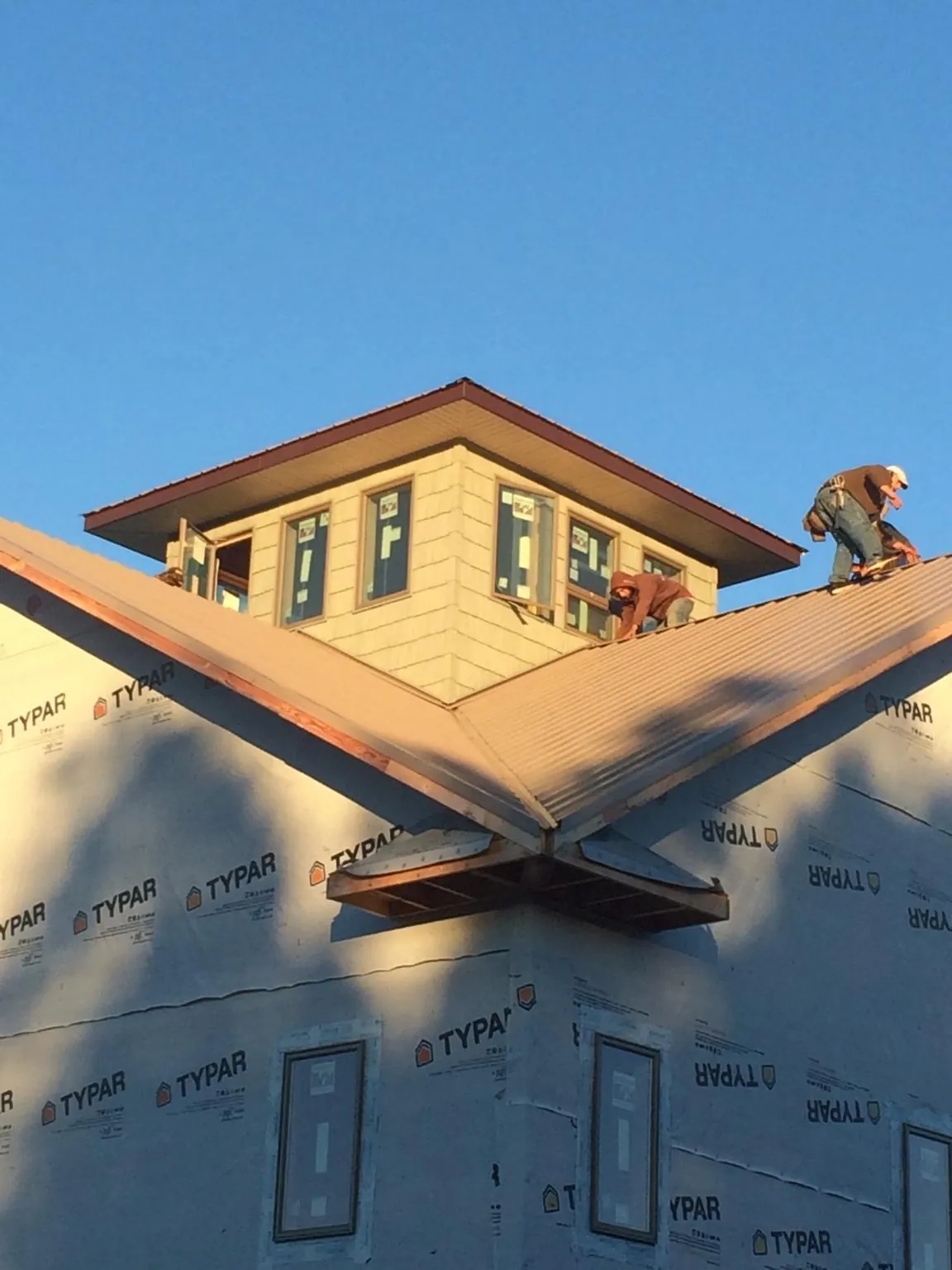 Roofers working around a rooftop cupola on a new metal roof at sunset — Roof Waterproofing in Youngsville by Roofing Brothers